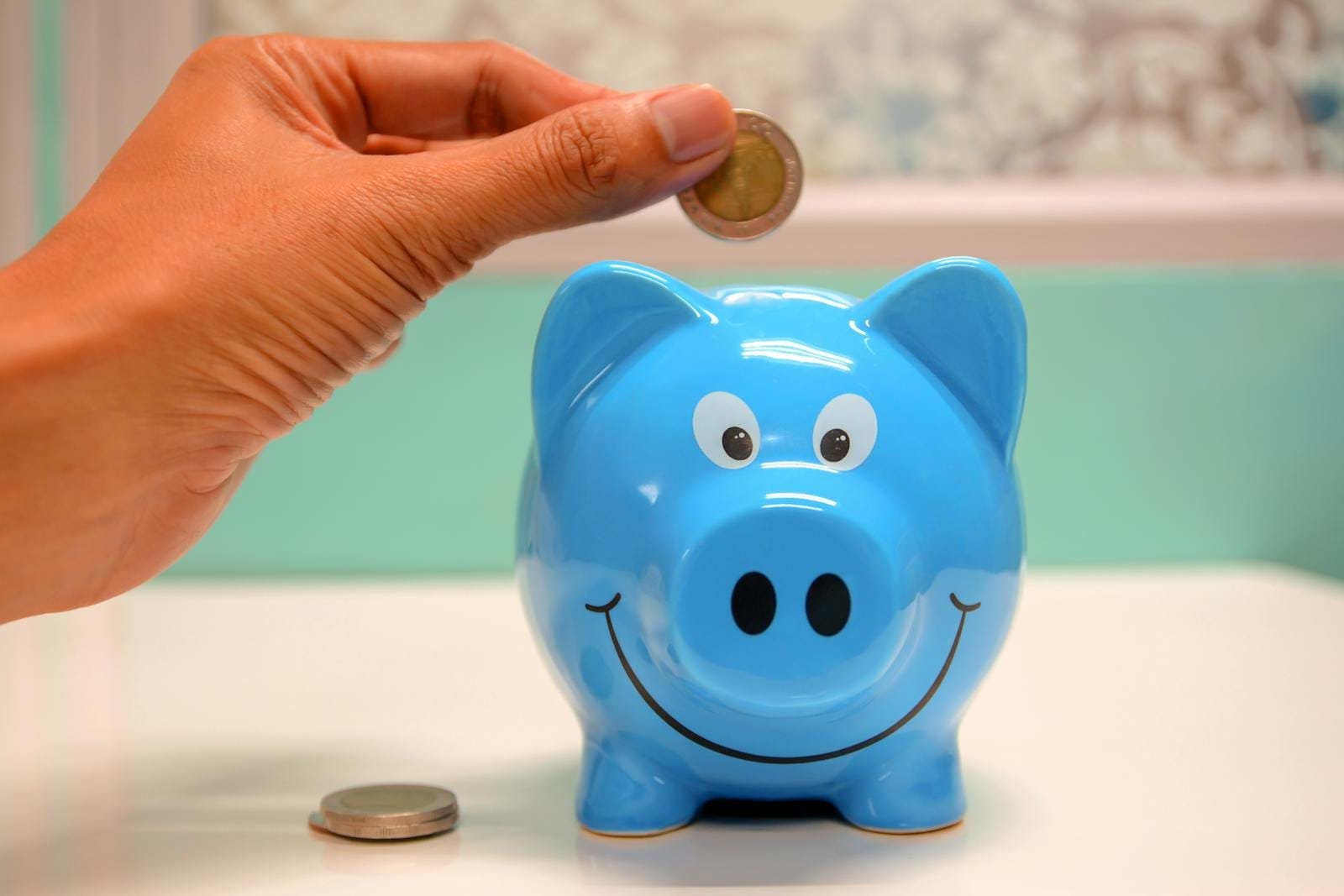 Mano insertando una moneda en una alcancía azul para ahorrar y administrar el dinero.